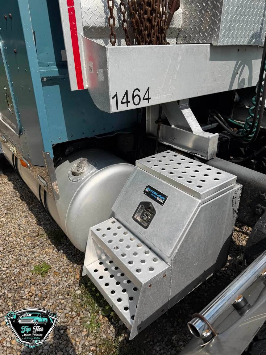 A polished aluminum fuel tank and step box on a semi truck frame