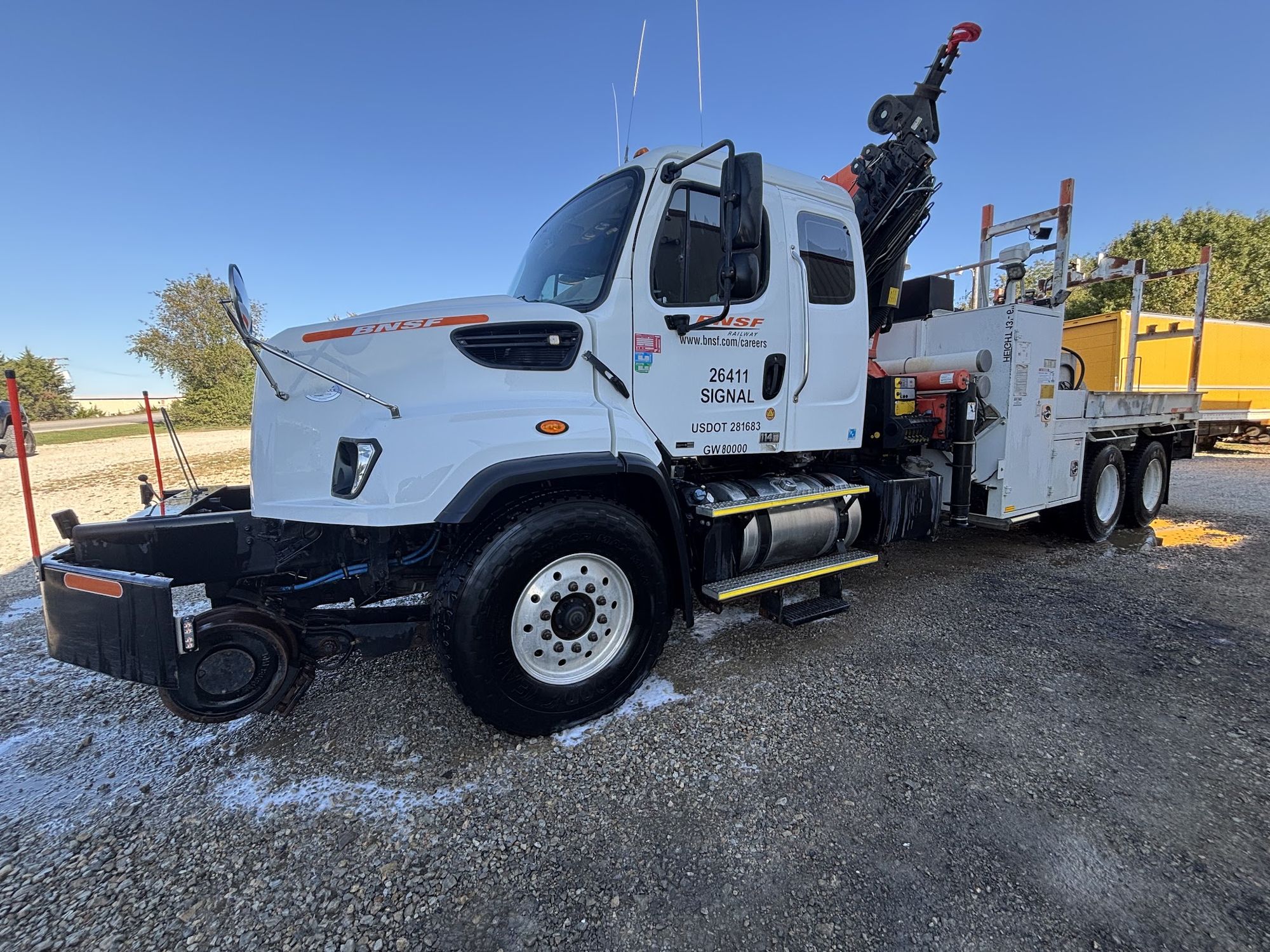 A freshly washed white fleet service truck with a crane bed, parked on gravel under a clear sky