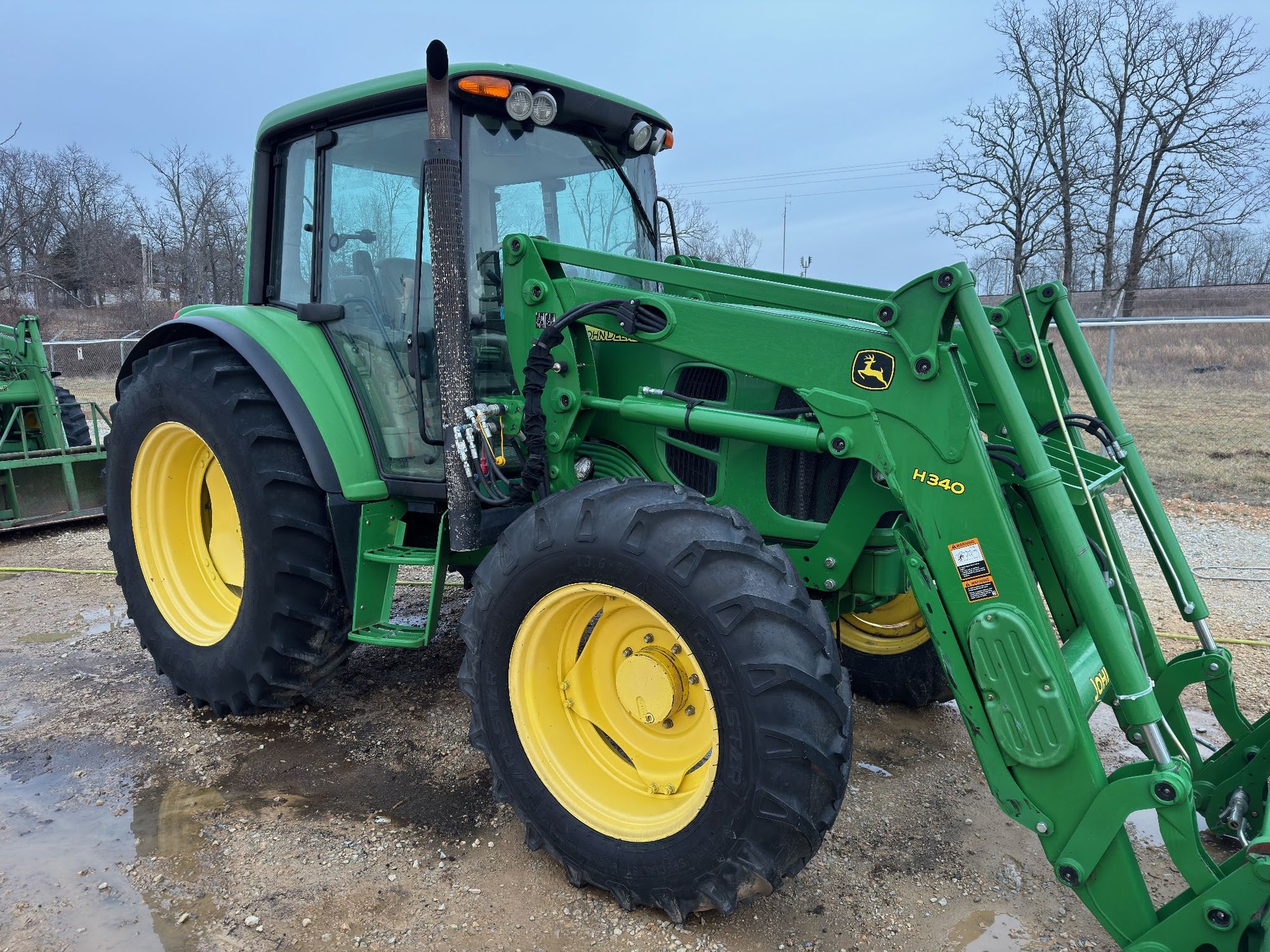 A green John Deere tractor with a front loader, washed clean, parked outside on gravel